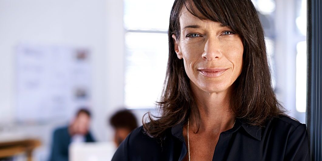 A Woman Standing In The Doorway To Her Office With Colleagues In The Background