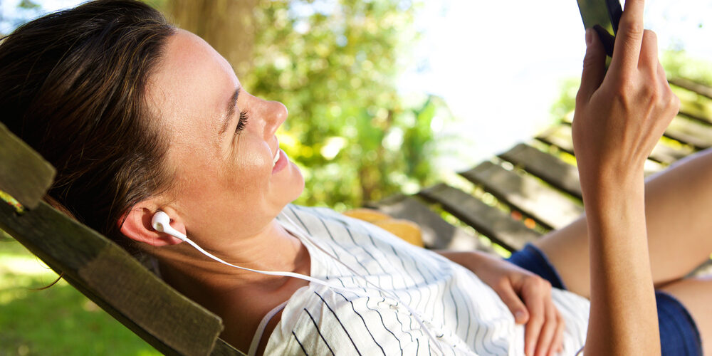 Relaxed Young Woman Lying On Hammock Outdoors And Listening To Music On Mobile Phone By Mimagephotography Via Shutterstock